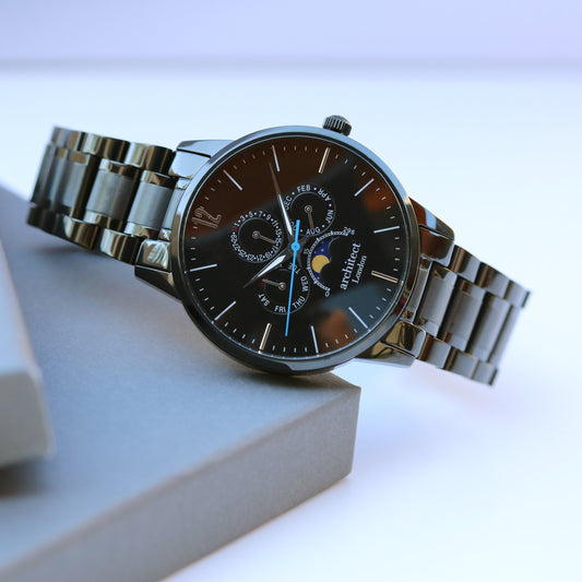 Silver watch with a black face on a light gray surface