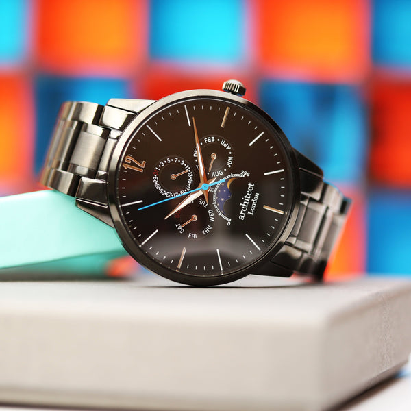 Silver watch with a black face on a white surface with a colorful geometric background