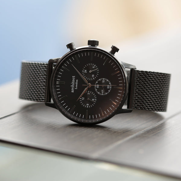 Black watch with mesh strap on a reflective surface