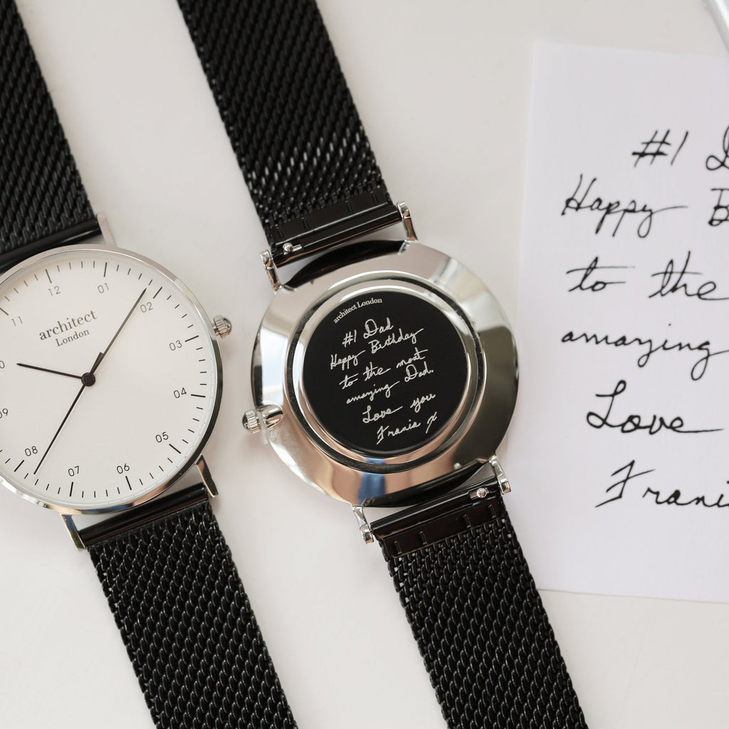 Two watches with black mesh straps on a white surface with handwritten text.