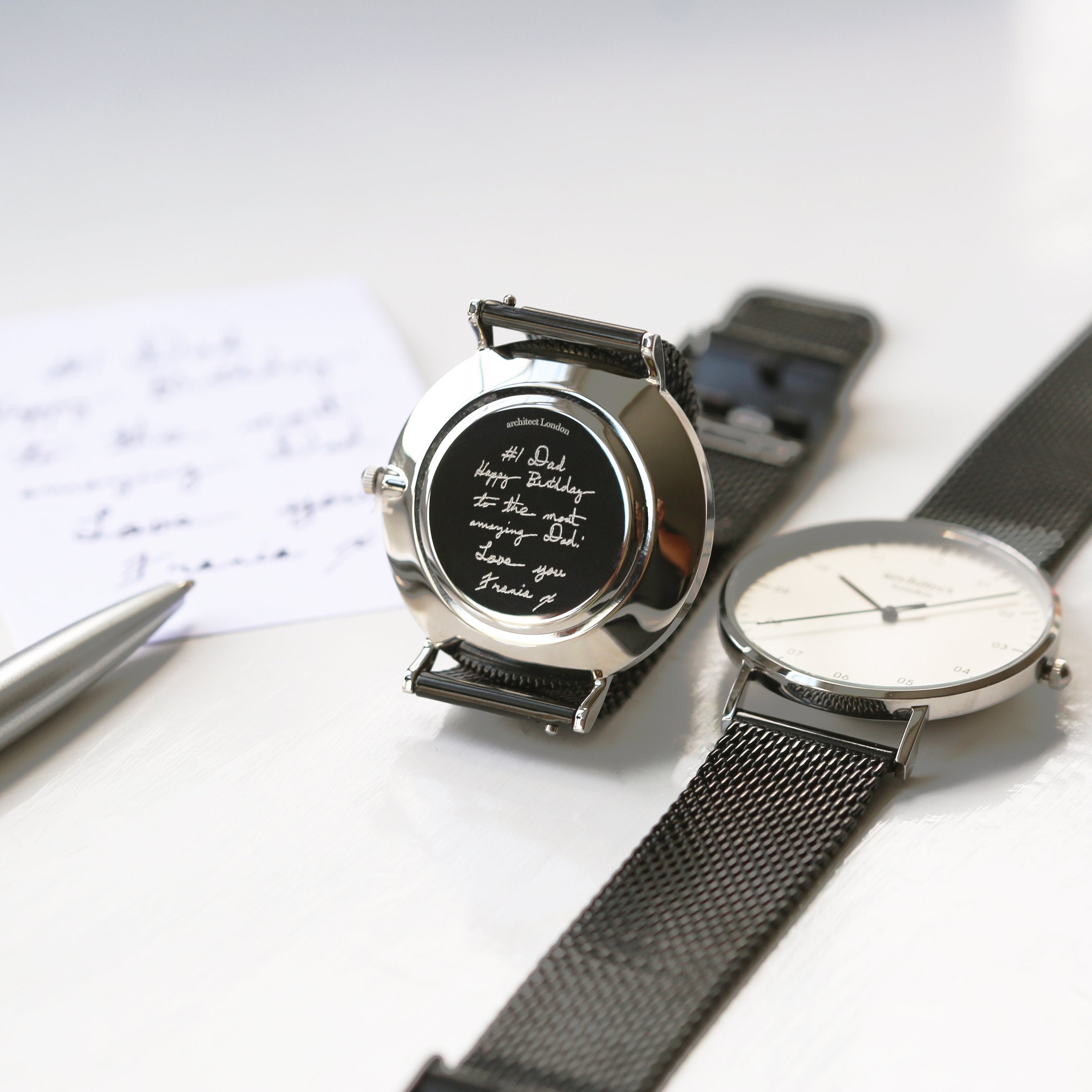 Two watches with black and silver straps on a white surface.

