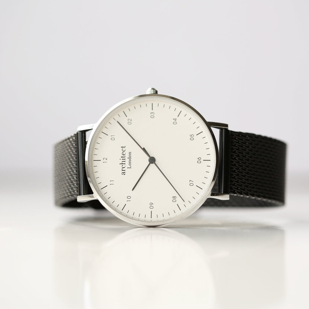 Watch with a black mesh strap and white dial on a light gray background