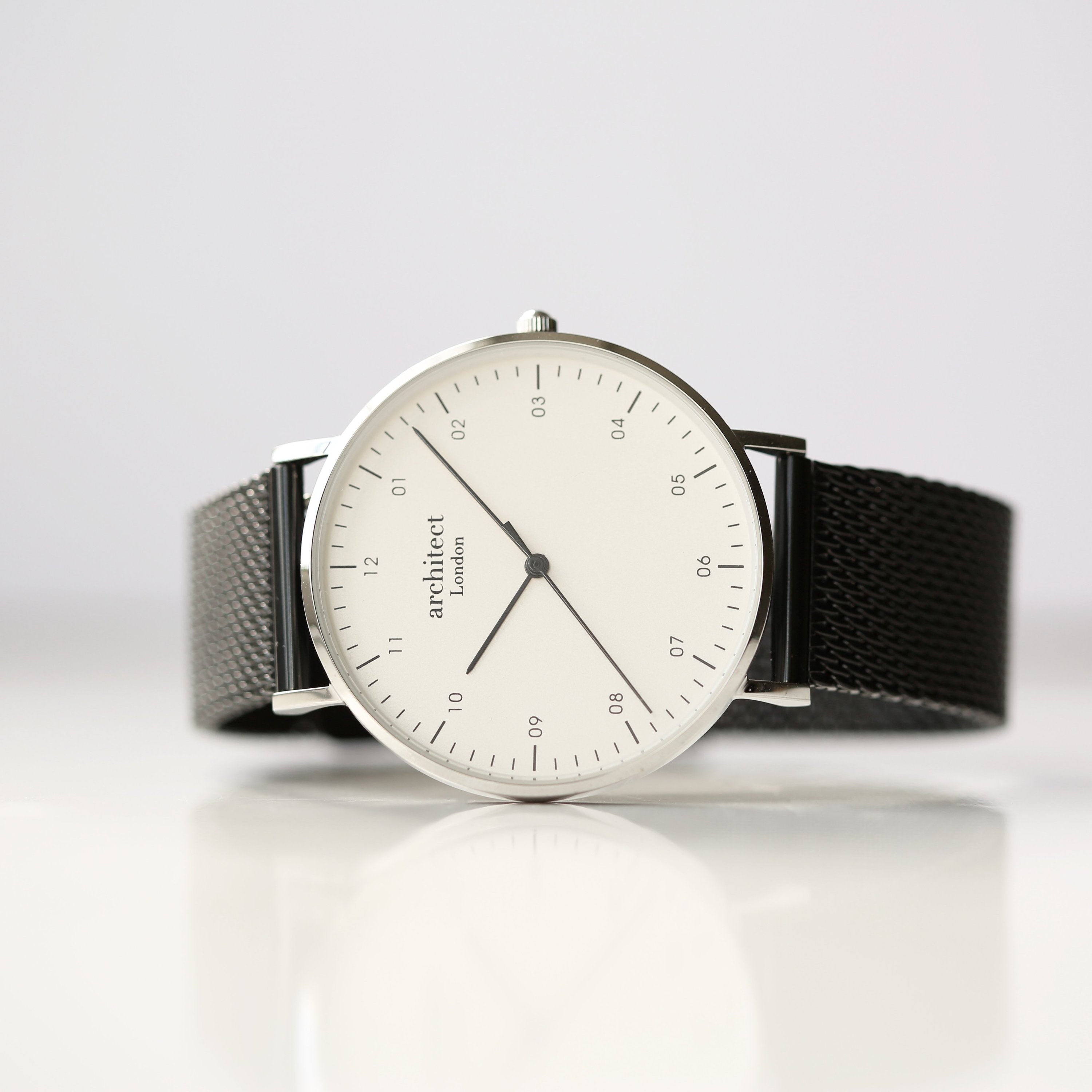Watch with a black mesh strap and white dial on a light gray background