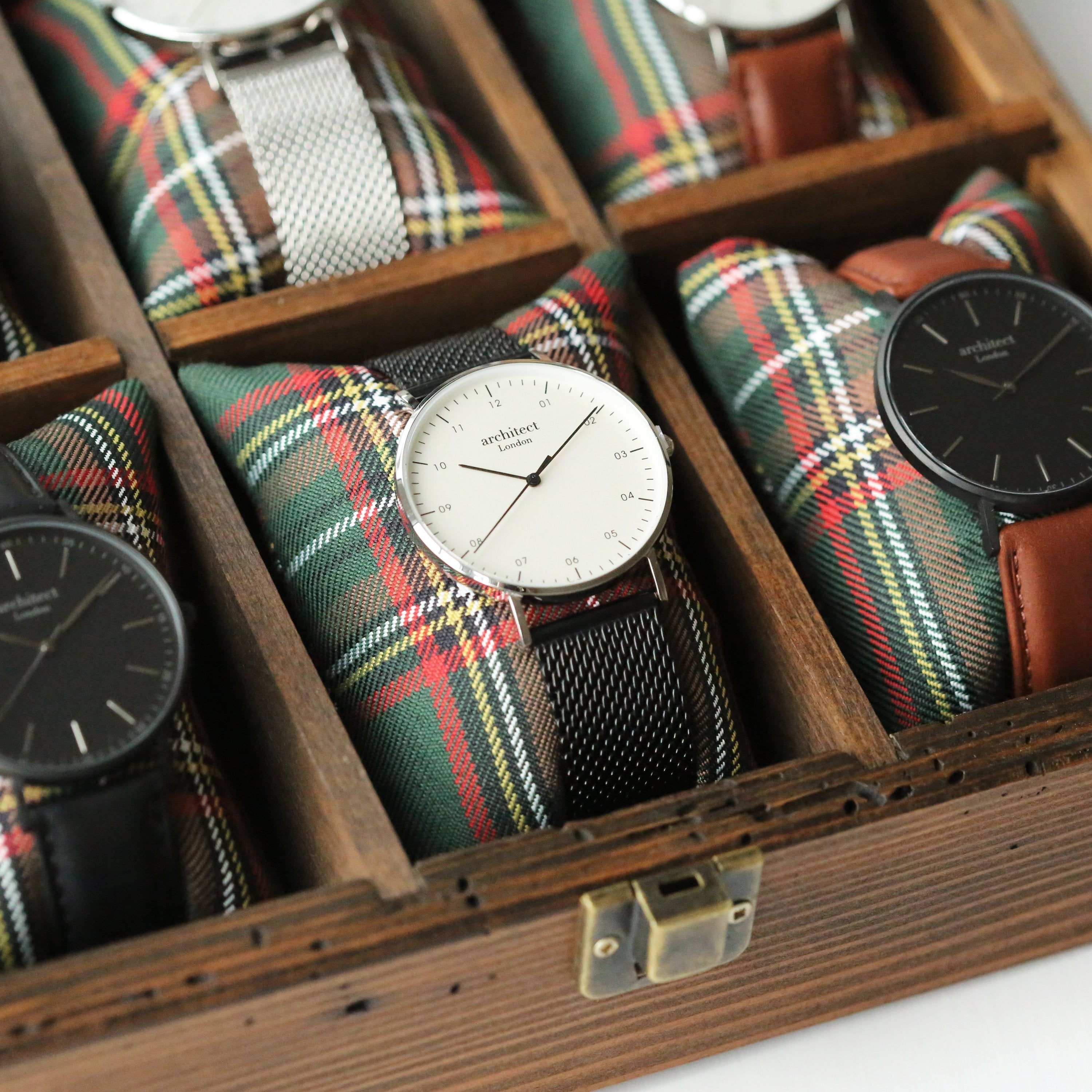 Collection of watches with plaid straps in a wooden display case.