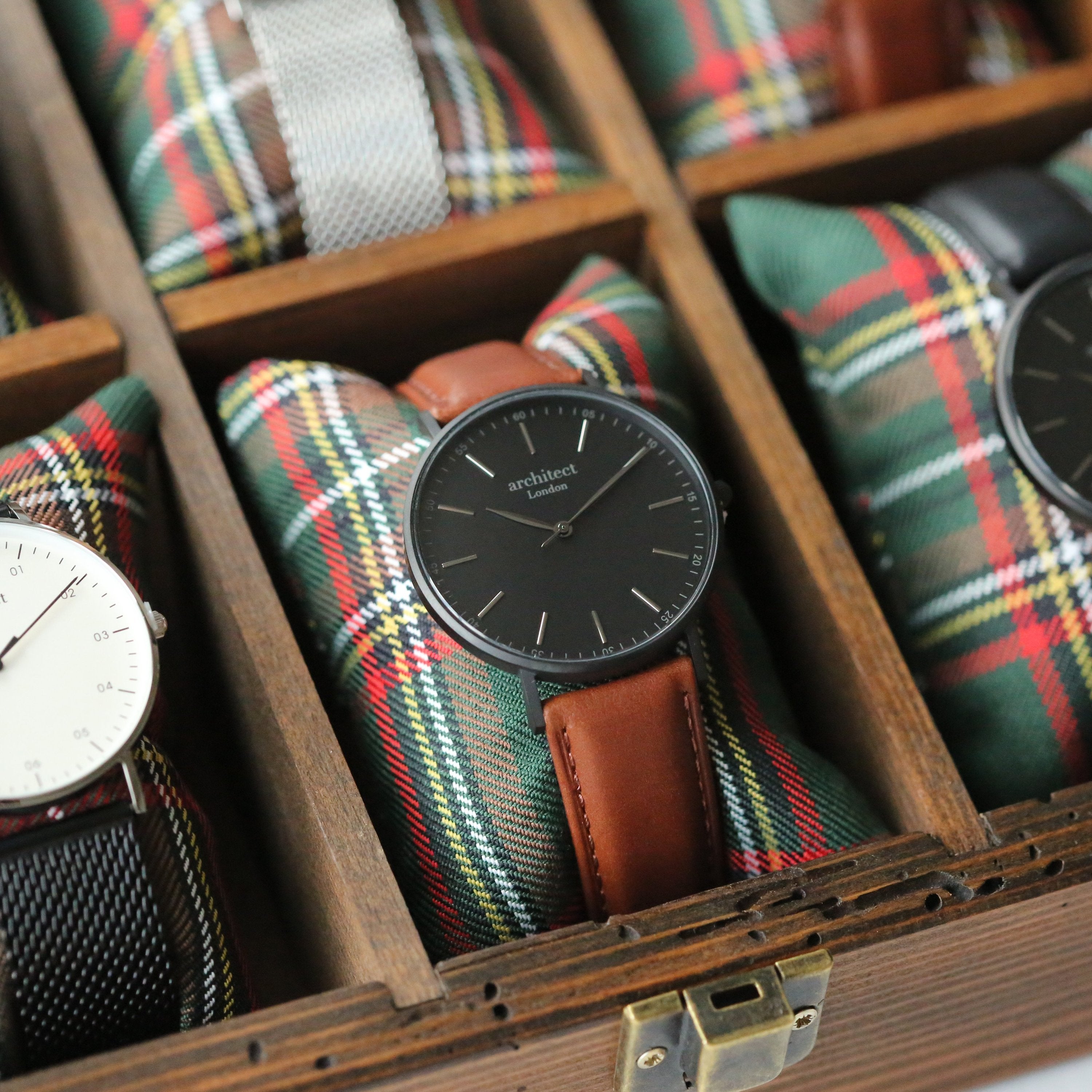 Watch with brown leather strap and black dial in a wooden display case with plaid fabric.