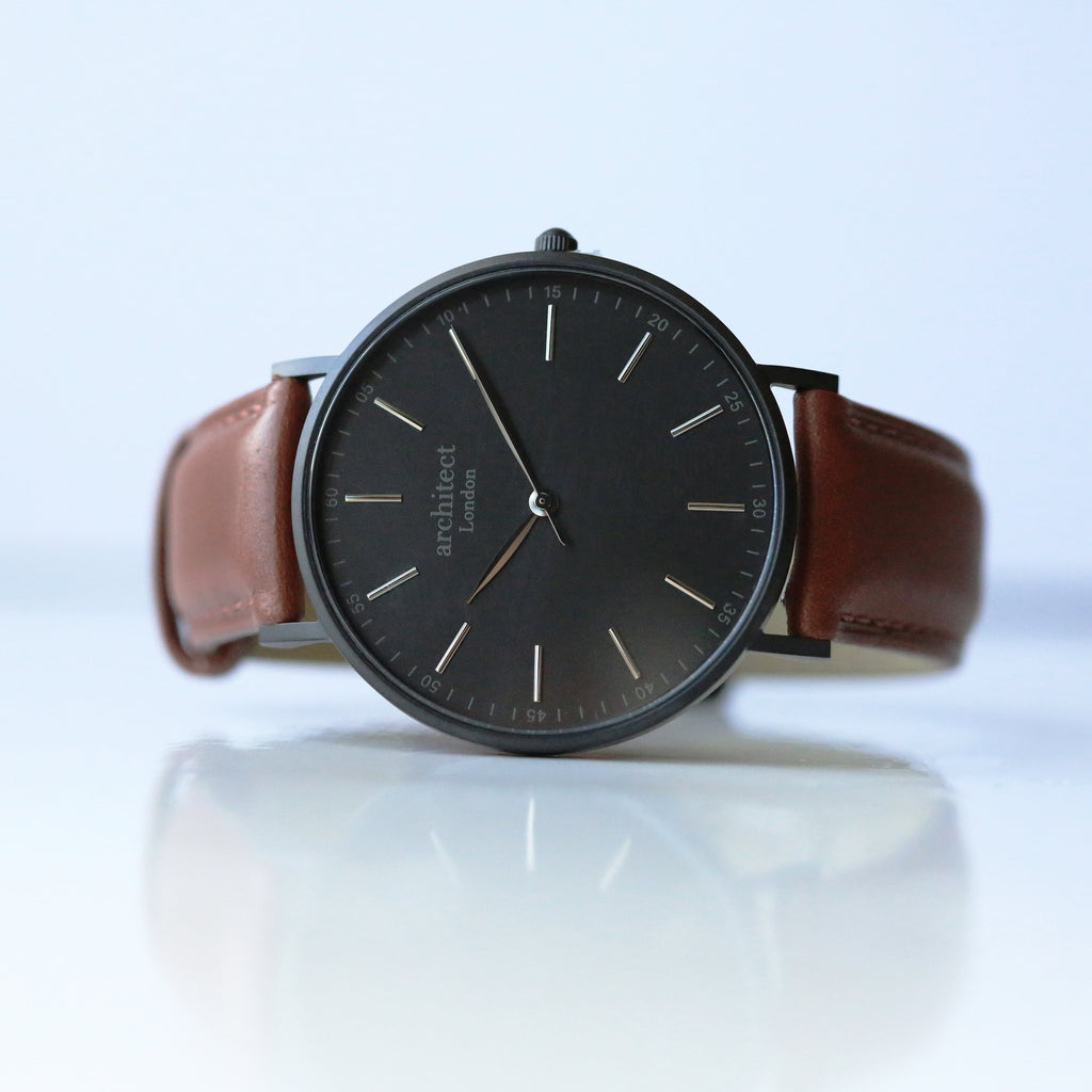 Watch with a brown leather strap and black dial on a white background