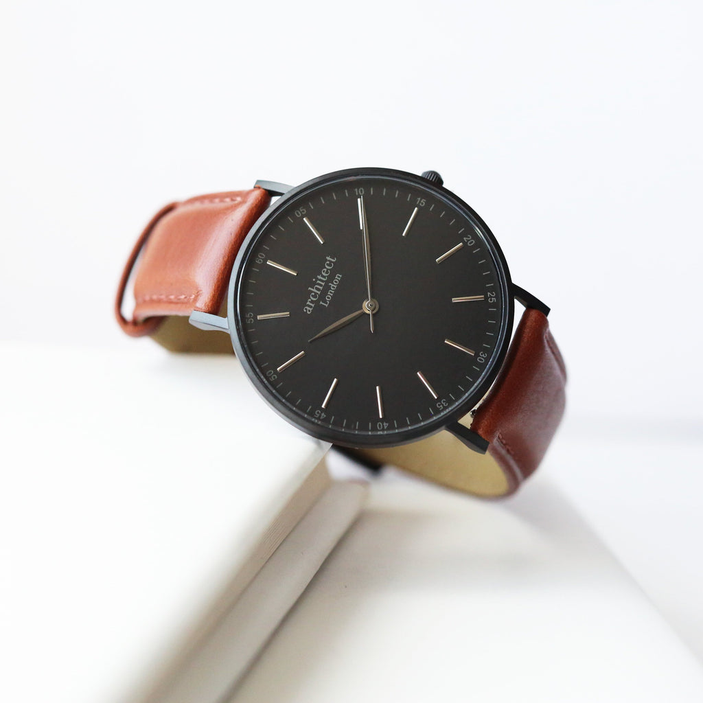 Watch with black dial and brown leather strap on a white background