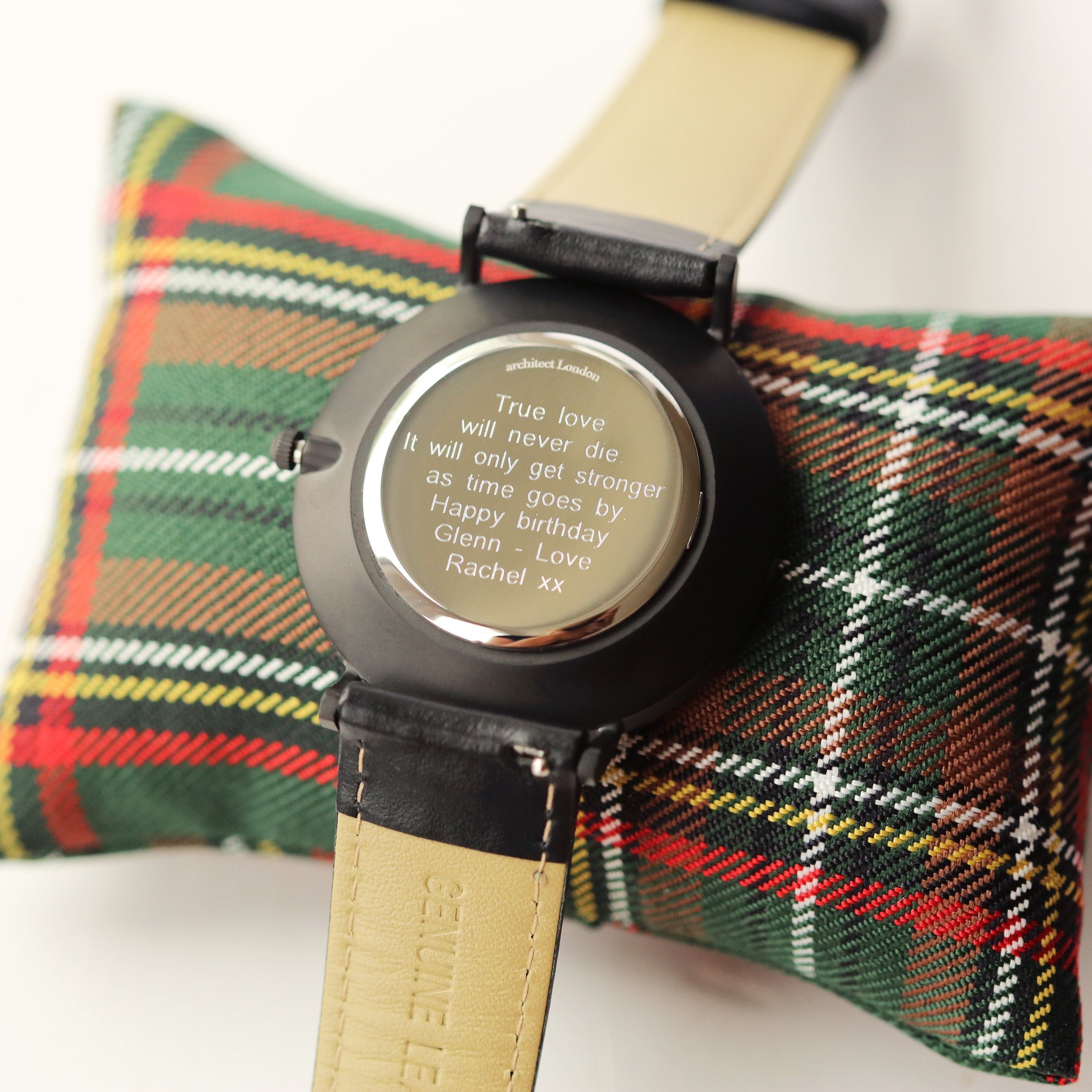 Watch with black strap and dark face displayed in a wooden box with plaid fabric