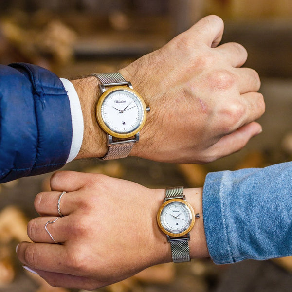 Two people wearing gold watches with mesh bands against a blurred background