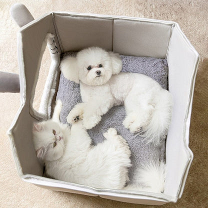 Two white dogs lying in a pet bed on a carpeted floor.